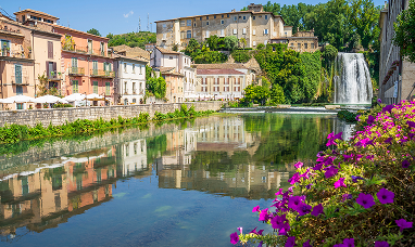 Veduta del Castello ducale Boncompagni Viscogliosi di Isola dei Liri,  con la Cascata Grande al centro del paese, edifici storici colorati riflessi nel fiume e fiori in primo piano.