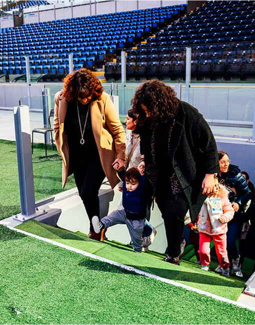 due volontarie accompagnano del bambini sul prato di una campo da calcio