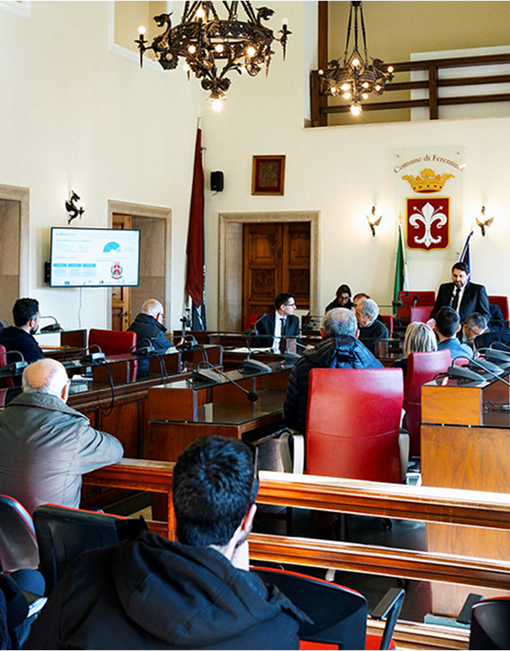 Incontro istituzionale con partecipanti seduti attorno a un tavolo e una presentazione visibile su schermo